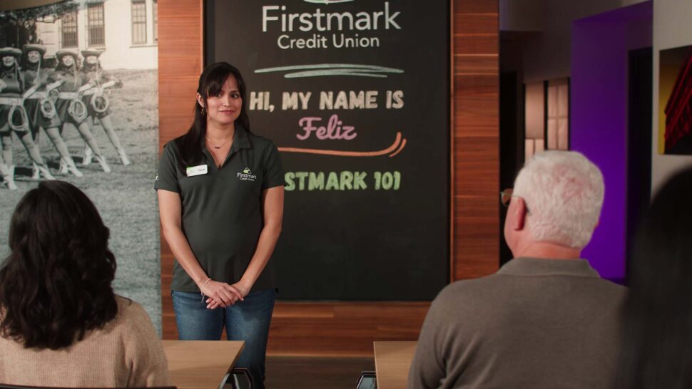 A woman named Feliz stands in front of a chalkboard at Firstmark Credit Union, presenting to a small seated audience