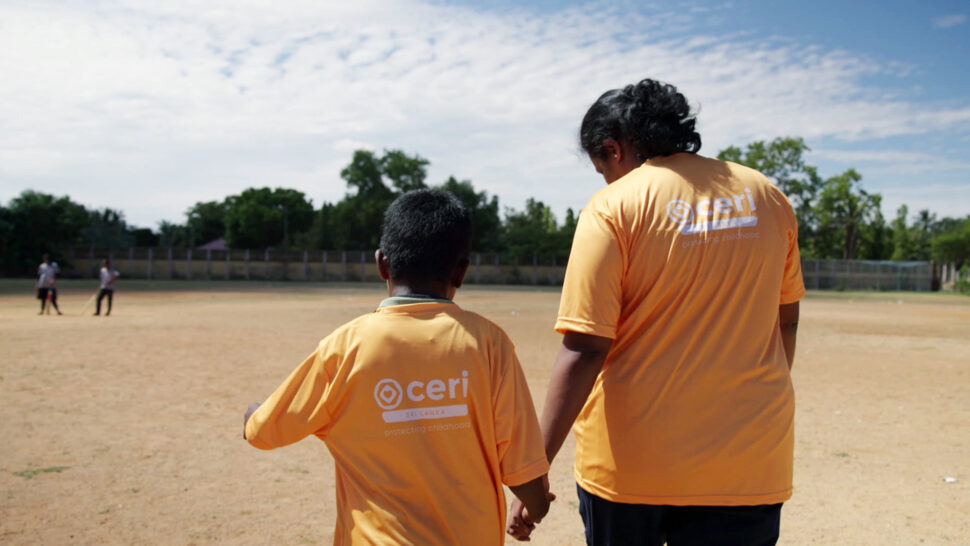 Adult and child wearing matching "ceri" shirts hold hands while walking across a sunny, open sports field.